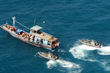 Two Border Protection Command boats surround a larger boat in the ocean.