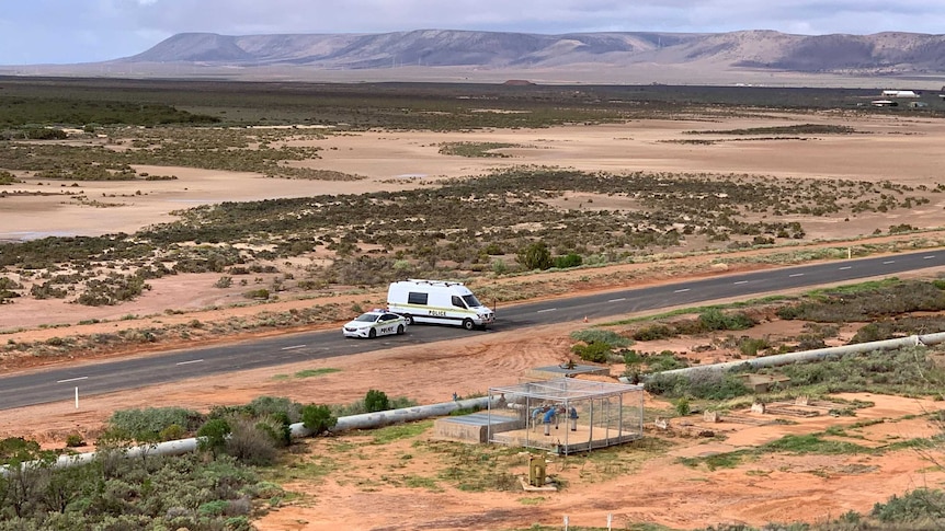 A police car and a van on a road with sand flats and hills behind