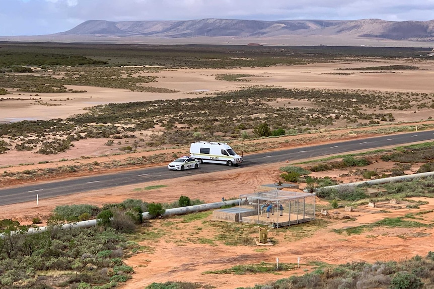 A police car and a van on a road with sand flats and hills behind