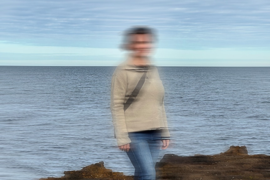 An undintifiable woman stands on rocks with the ocean in the background.