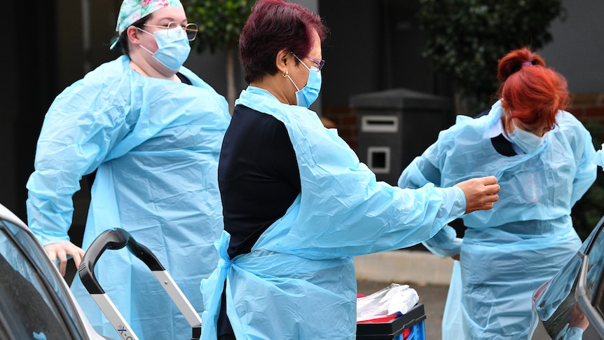 Three workers in blue PPE gowns prep to go inside an aged care home.