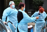 Three workers in blue PPE gowns prep to go inside an aged care home