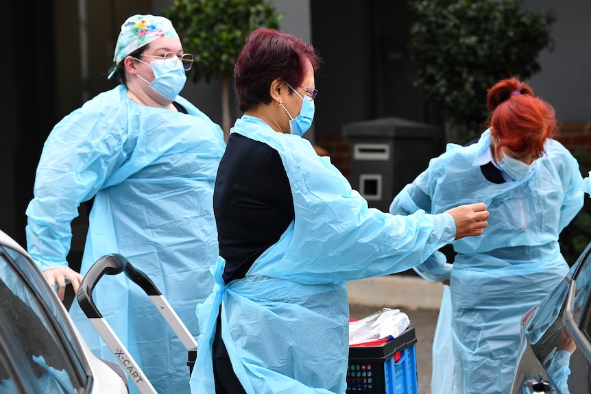 Three workers in blue PPE gowns preparing to enter a geriatric care facility