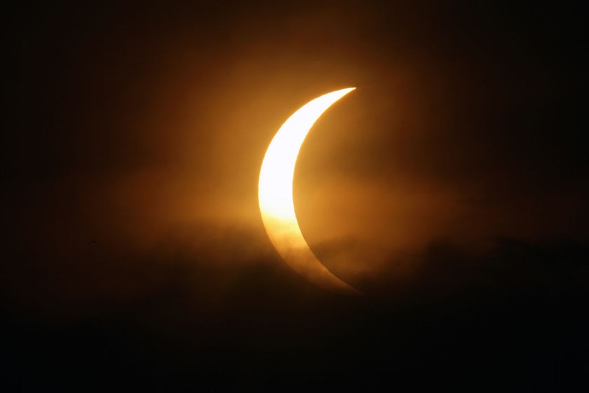 The moon passes between the sun and earth in monsoon clouds during a solar eclipse in Delhi