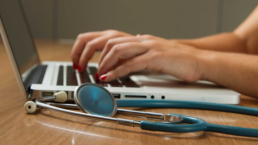 Close-up of a woman typing on a laptop computer with a stethoscope next to her