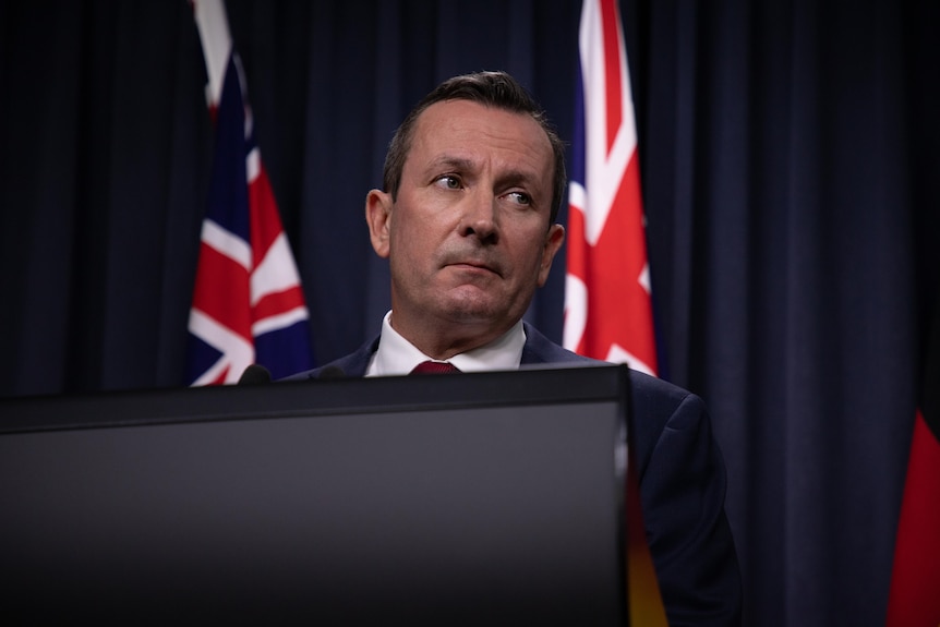 A close up of Mark McGowan speaking at a lecturn with a flag in the backdrop
