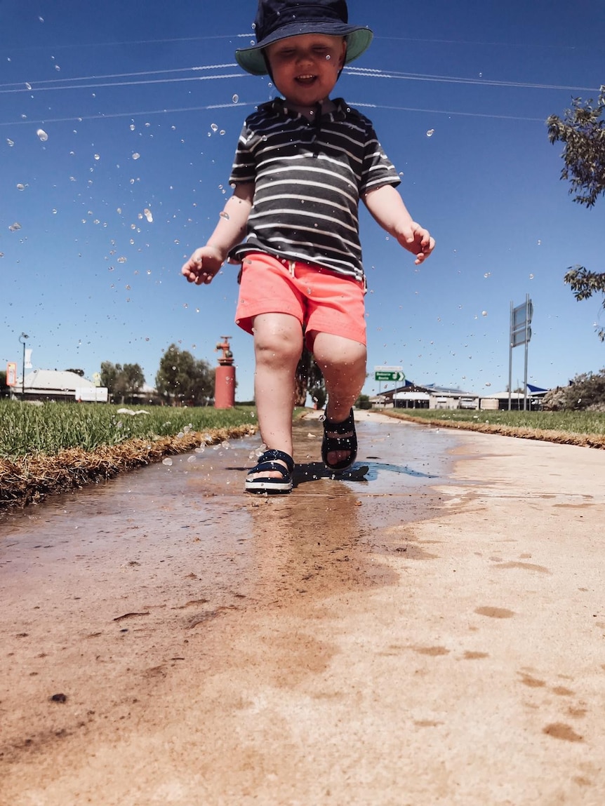 A toddler plays in a puddle.