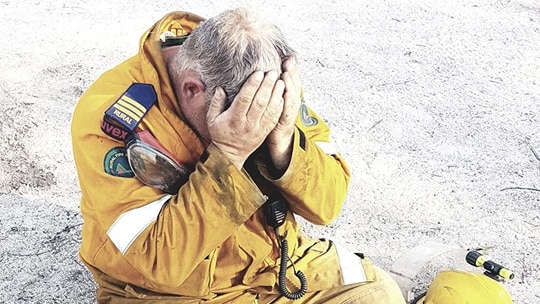 Ballandean rural firefighter Aaron Cox sitting on the ground with his head in his hands.