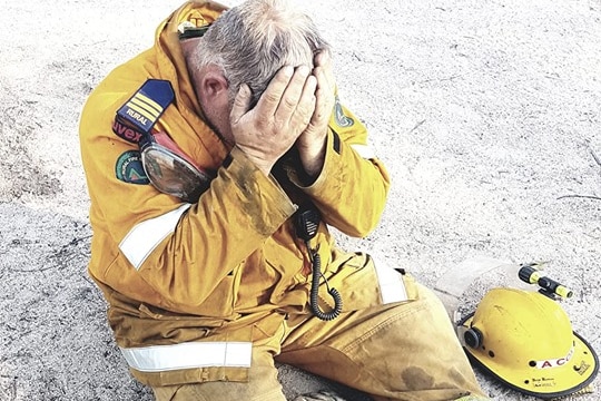 Ballandean rural firefighter Aaron Cox sitting on the ground with his head in his hands.