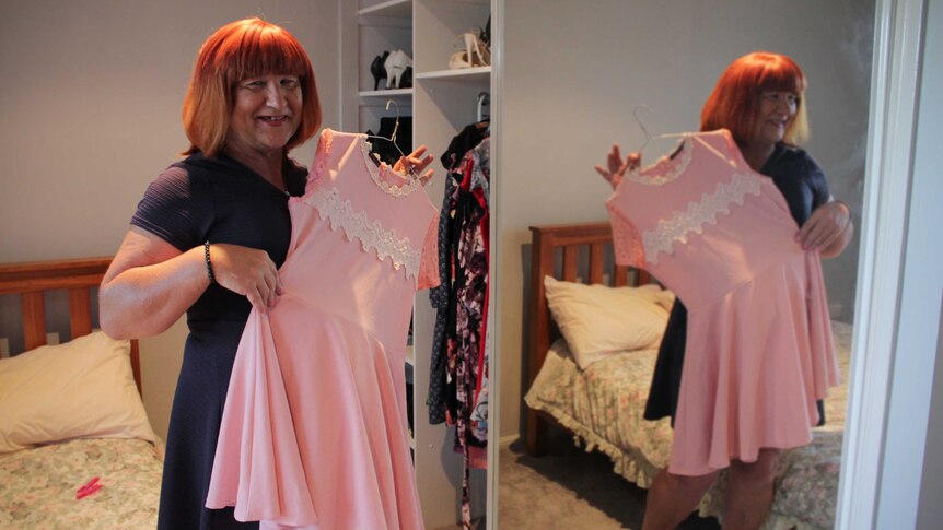Emily Wells standing in her bedroom, holding up a pink dress to her.