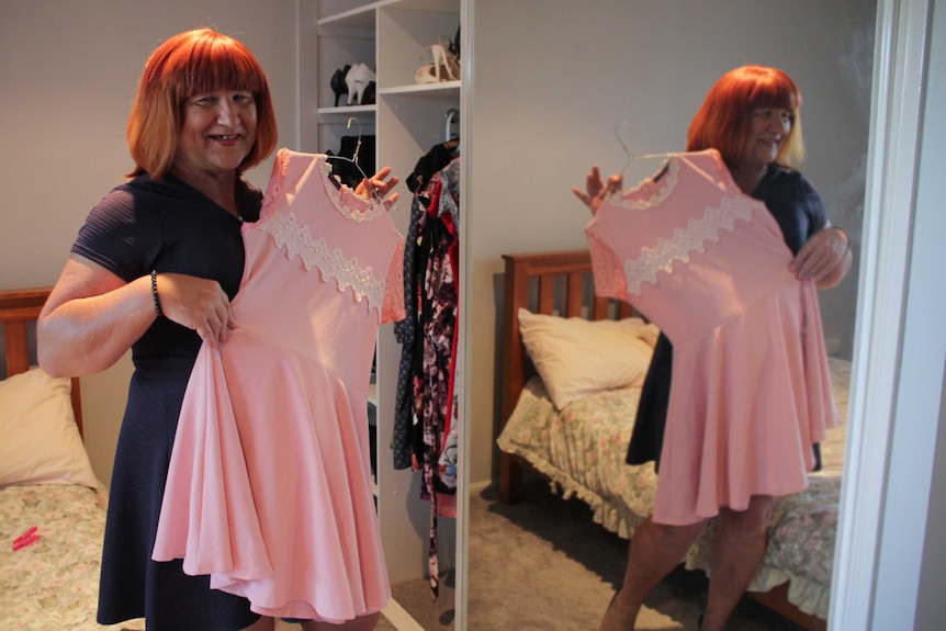 Emily Wells standing in her bedroom, holding up a pink dress to her.