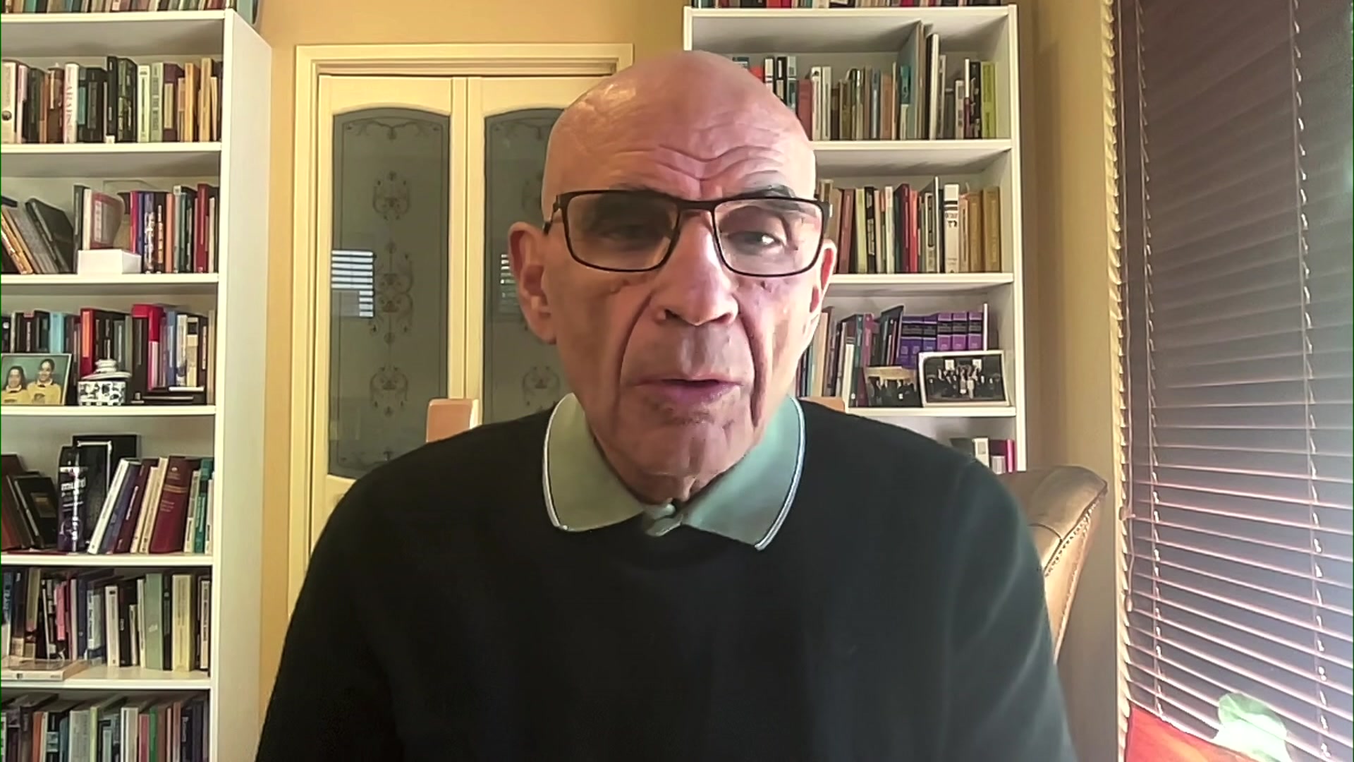 A middle-aged man in glasses sits in fornt of book cases and a set of French doors in a home office.