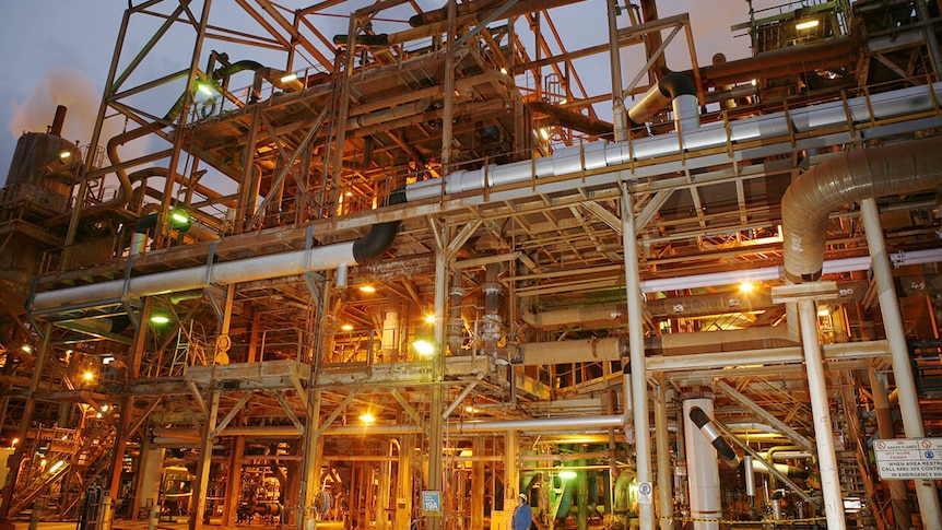 A lot of silver metal pipes at a refinery at dusk.