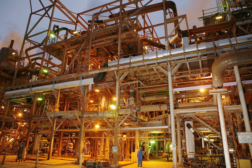 A lot of silver metal pipes at a refinery at dusk.