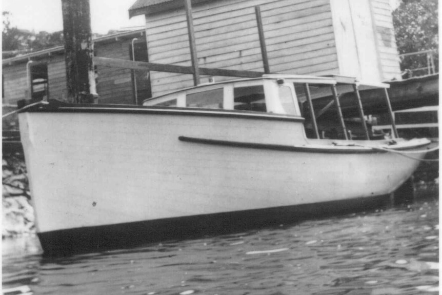 A black and white photo of a small wooden boat against a wharf