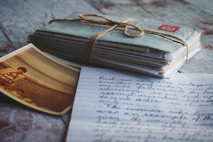 A stack of handwritten envelopes tied with string, sits beside a handwritten letter and a photograph.