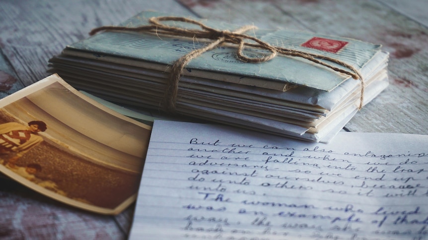 A stack of handwritten envelopes tied with string, sits beside a handwritten letter and a photograph.