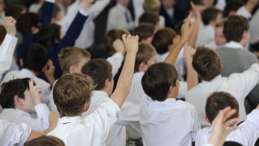 The back of teen boys' heads at a school assembly with a few with their hands up