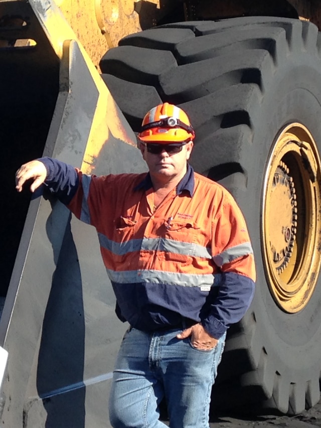 Greg Halloran wears a helmet and stands next to a large mining vehicle