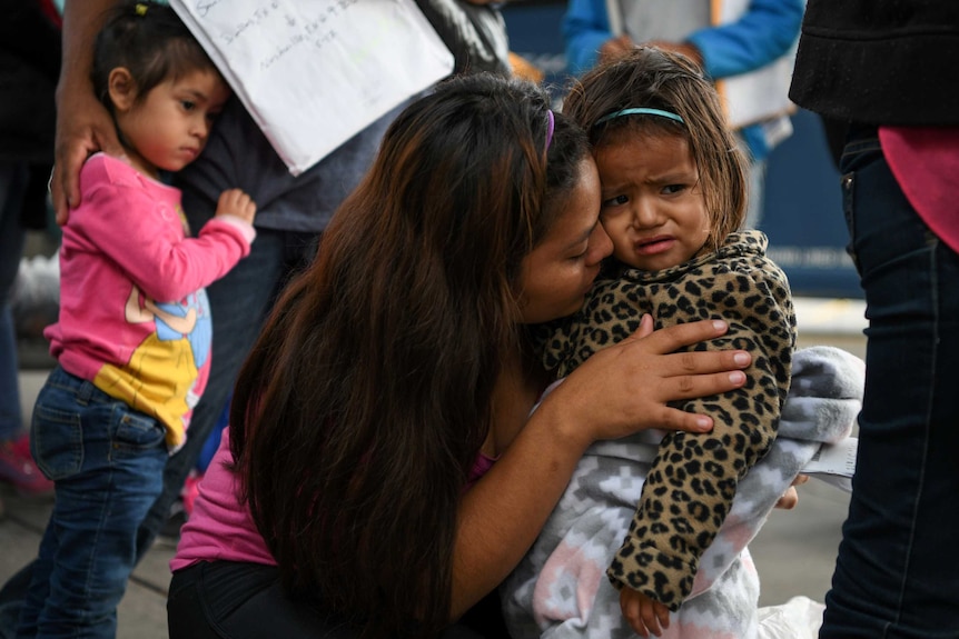 An asylum seeker embraces her young daughter who appears to be upset.