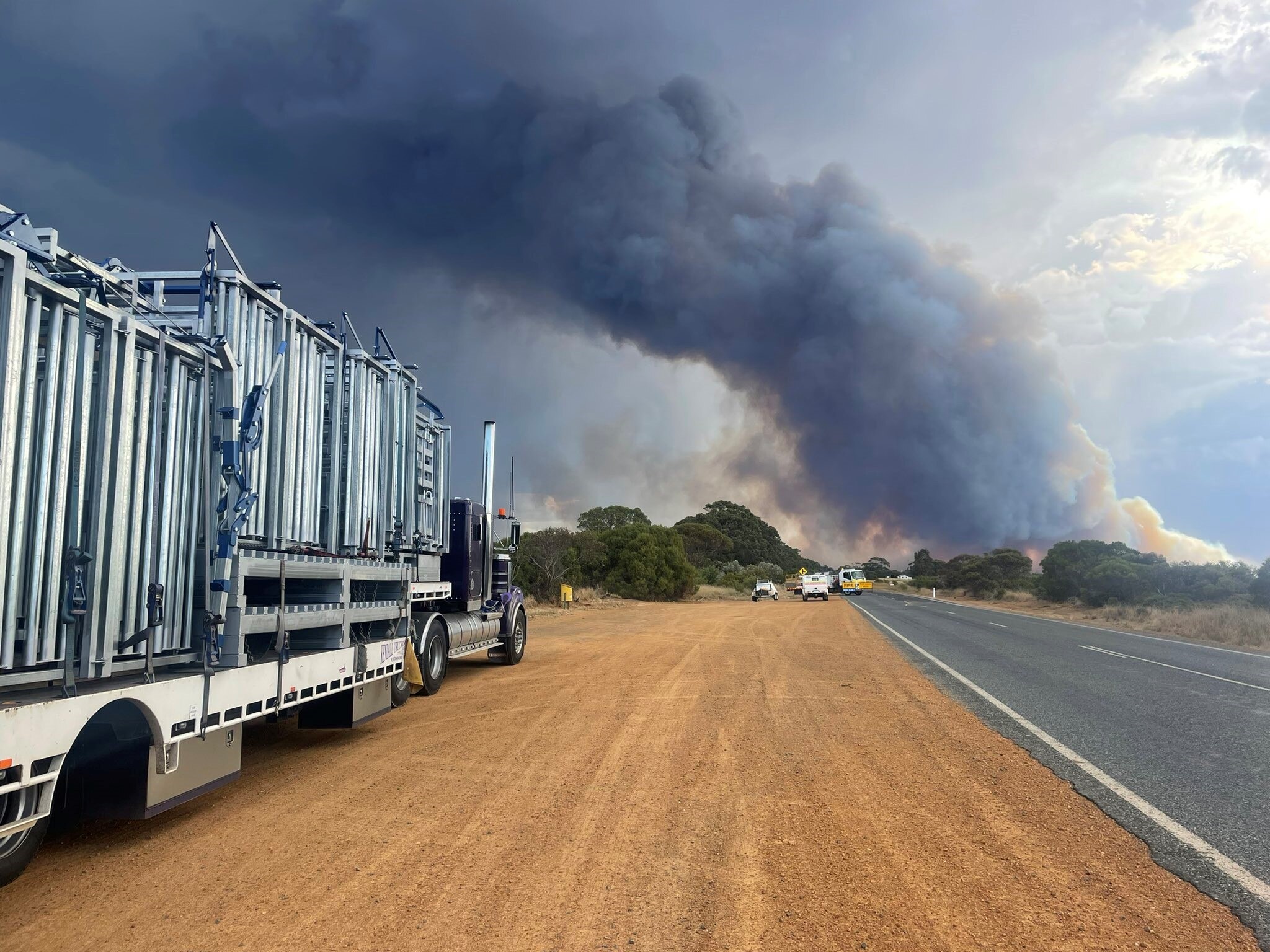 A truck parked on side of road near a bushfire. 