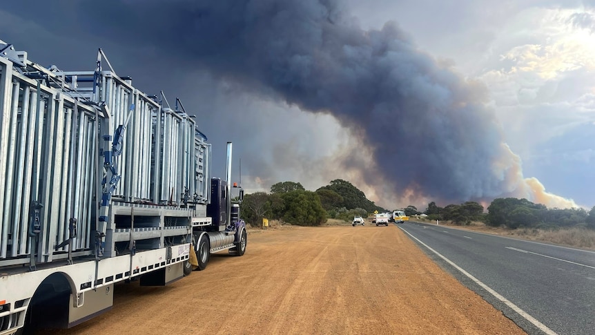 A truck parked on side of road near a bushfire.