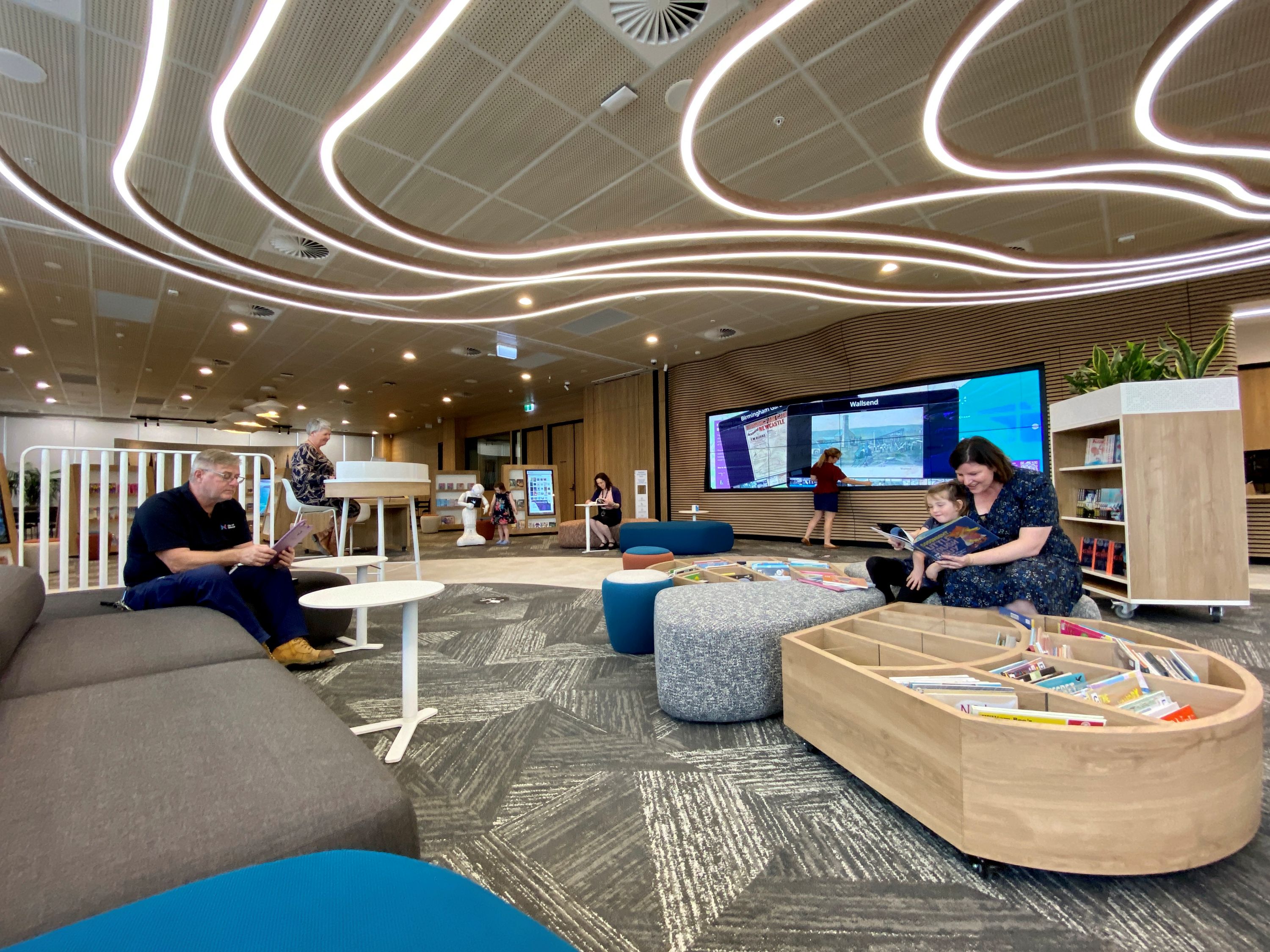 People sitting in a library filled with book bins, desks and sofas