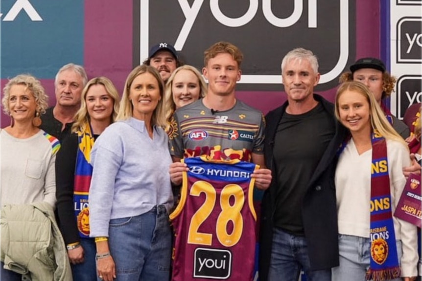brisbane lions player jaspa fletcher poses holding his jumper with his family