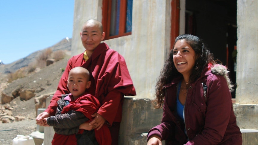 A woman sits outside a concrete building with a Tibetan monk and child.