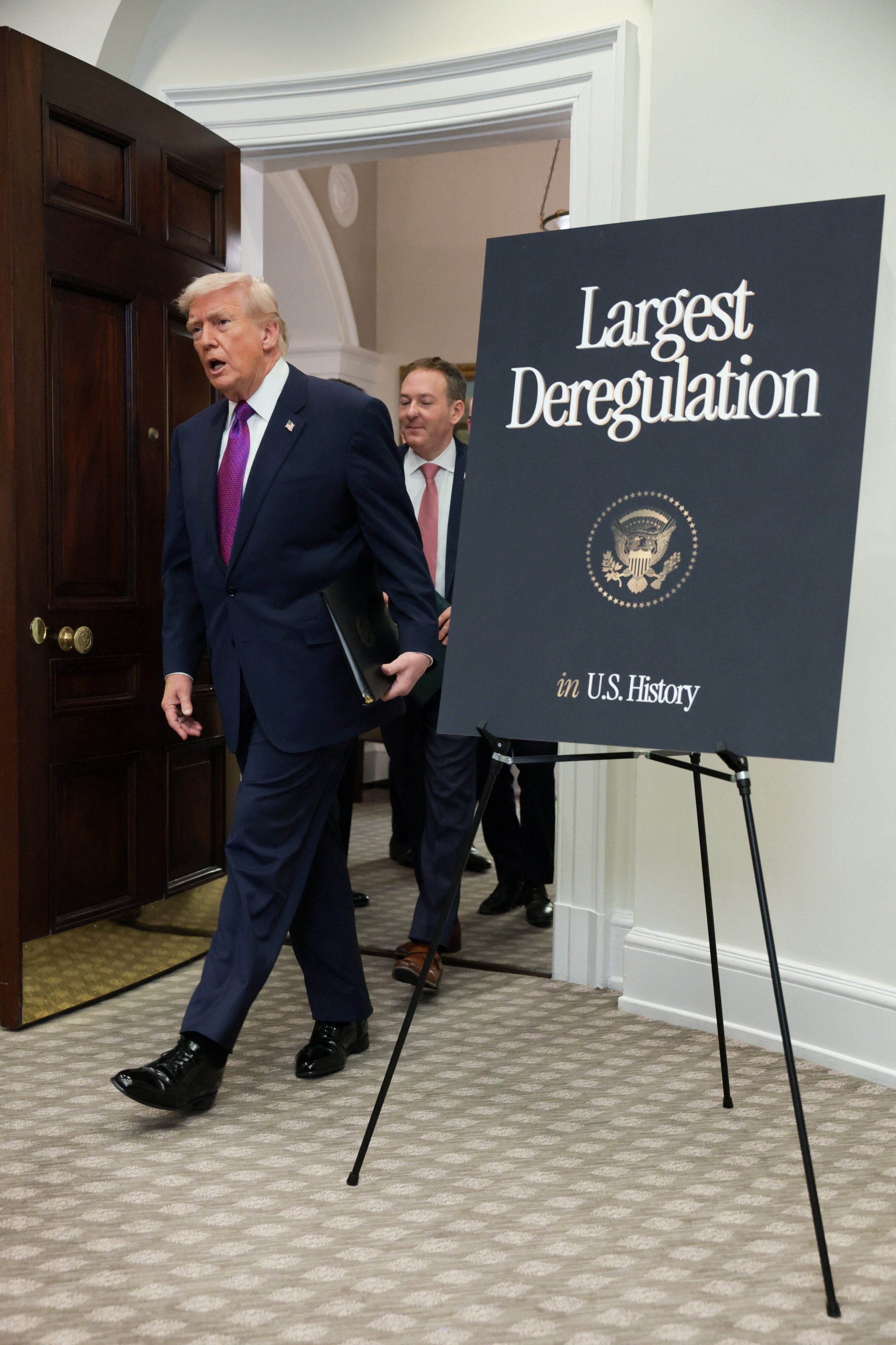 A man in a suit walks past a sign that says 'largest deregulation in U.S history'