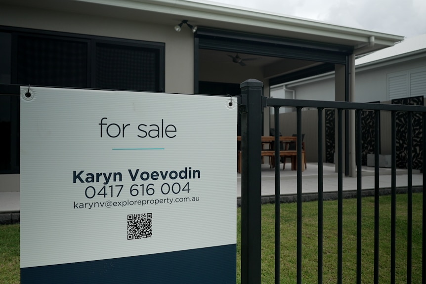 Un cartel de venta en una valla de metal negro frente a una propiedad