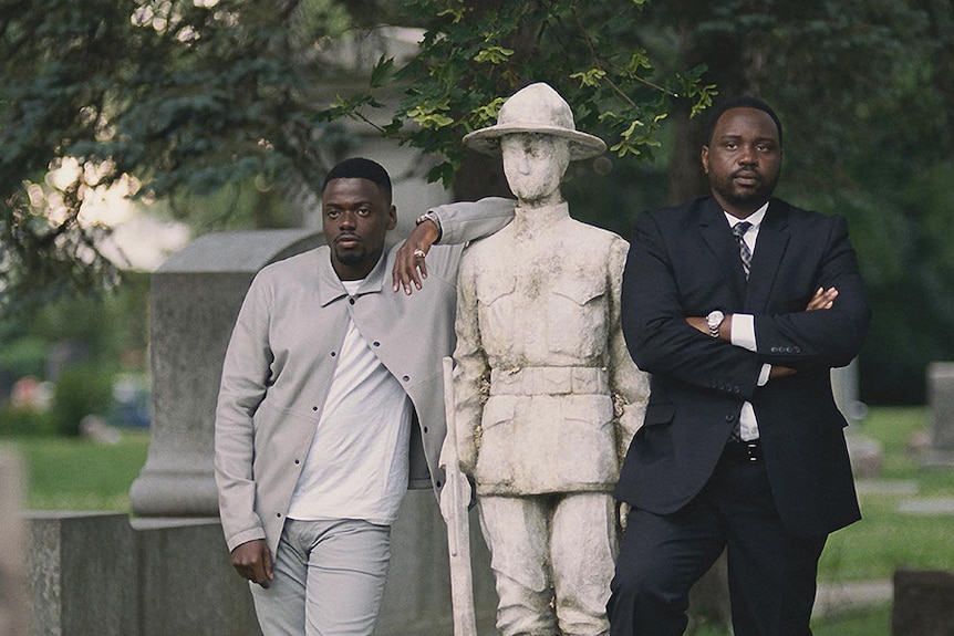 Colour still of Daniel Kaluuya and Brian Tyree Henry standing next to soldier statue in graveyard in 2018 film Widows.