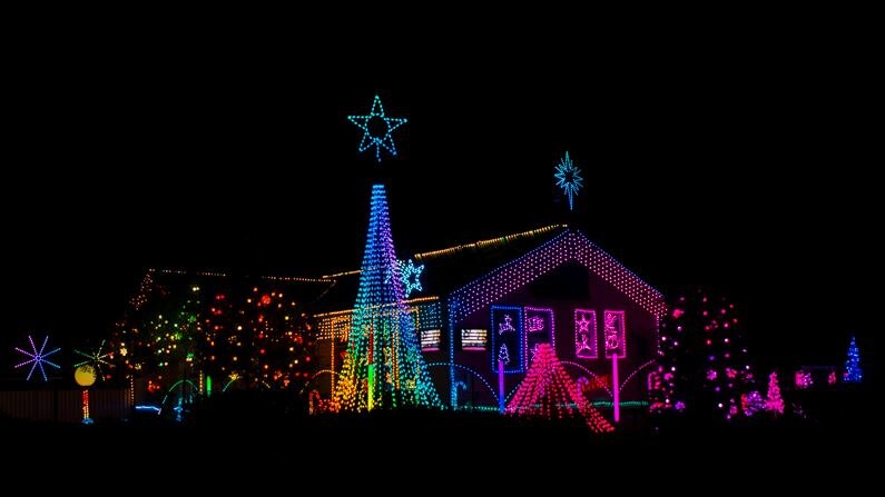 A night time shot of a house and garden lit up with rainbow coloured lights including stars and a Christmas tree