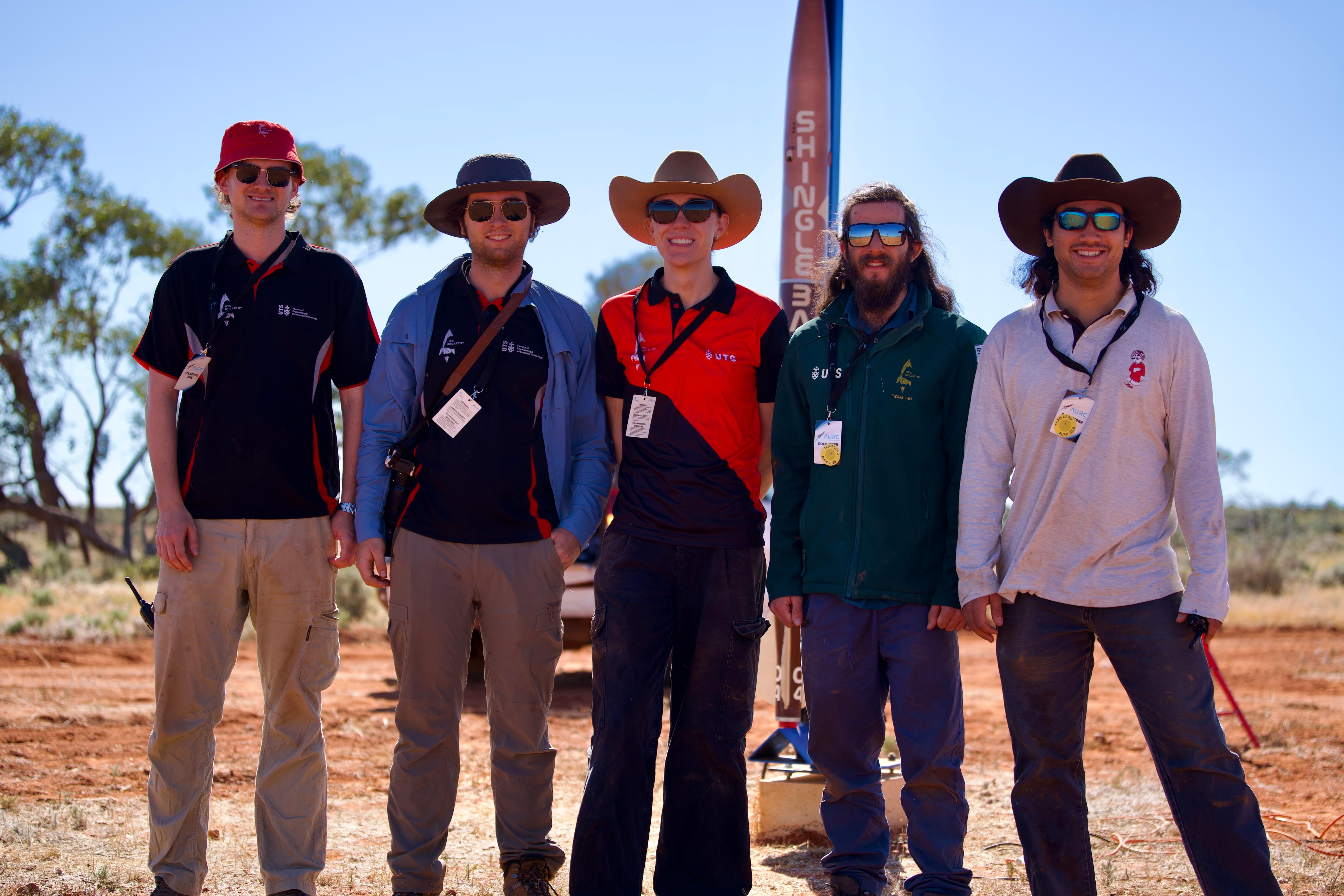 Five smiling young men, all in hats and sunglasses, standing on an outback property.