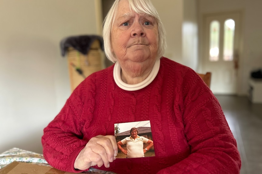 A woman has a concerned expresion on her face. She holds a photo of a man.