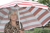 A woman stands underneath a breach umbrella in her backyard.