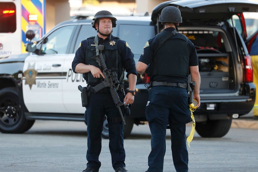 Two police officers holding guns stand outside