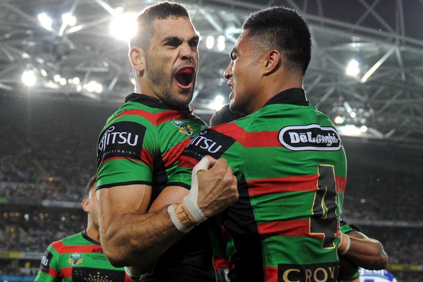 Rabbitohs NRL player celebrates with his team mates under a light-lit field