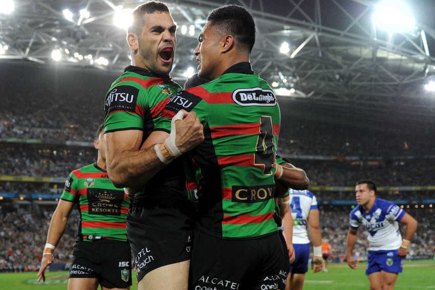 Rabbitohs NRL player celebrates with his team mates under a light-lit field