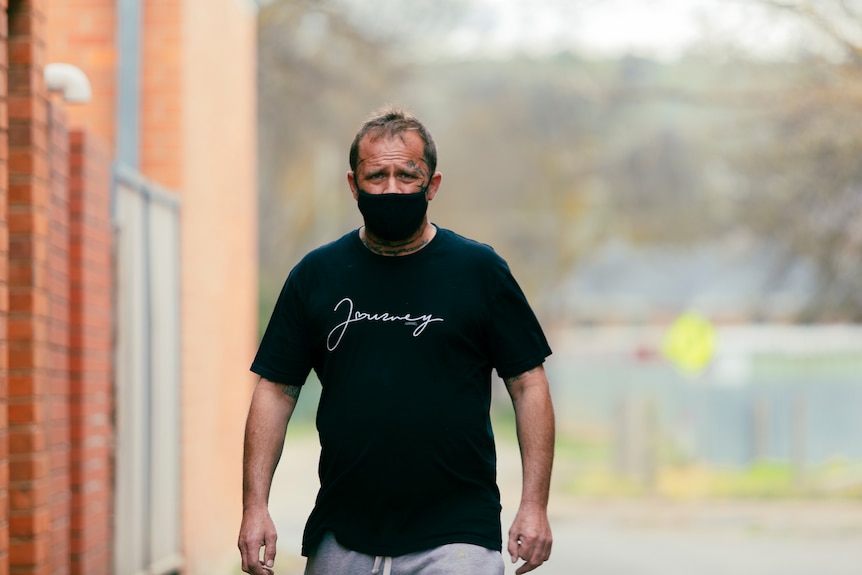 Brian Warton walks down a street, wearing a COVID face mask.