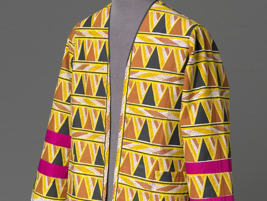 Colourful ceremonial jacket with yellow, black, ochre, and white patterns standing on a tailor's mannequin