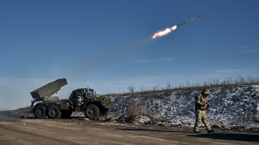 Ukrainian army grad multiple rocket launcher fires rocket as soldier walks nearby.