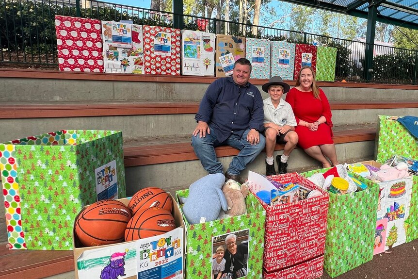 Todd Sheldon sitting next to his son Lachlan and Maitland MP Jenny Aitchison surrounded by wrapped boxes filled with presents. 