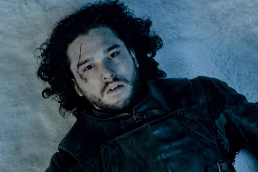Jon Snow's lifeless eyes stare into space as he rests on snow with blood trickling out of his body.