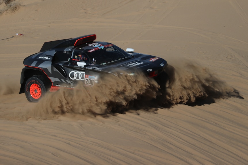 A black car drives through sand