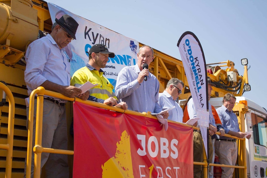 A group of man stand on top of a truck style vehicle, with politiical banners.