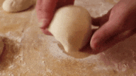 Two hands are holding a small ball of dough that's been kneaded until soft and smooth.
