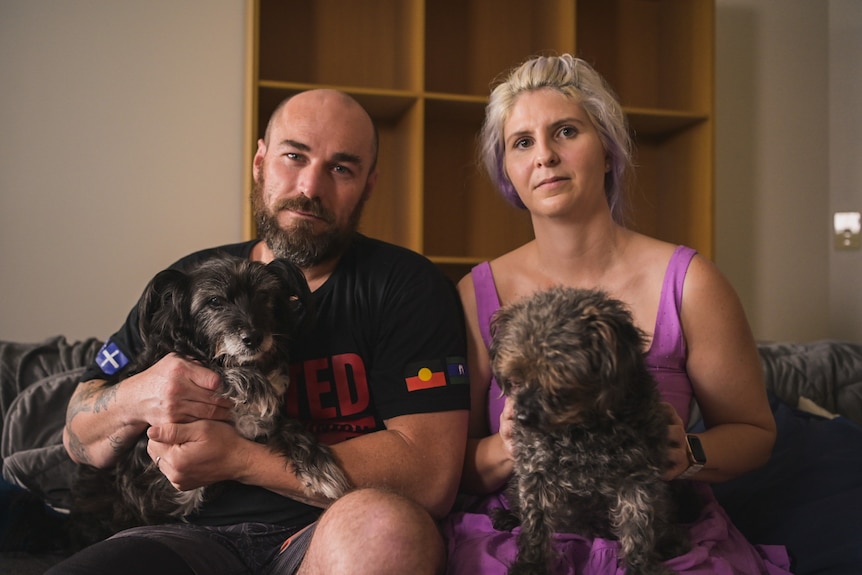 Dale Billett and Katie Havelberg sit on the couch with two dogs.