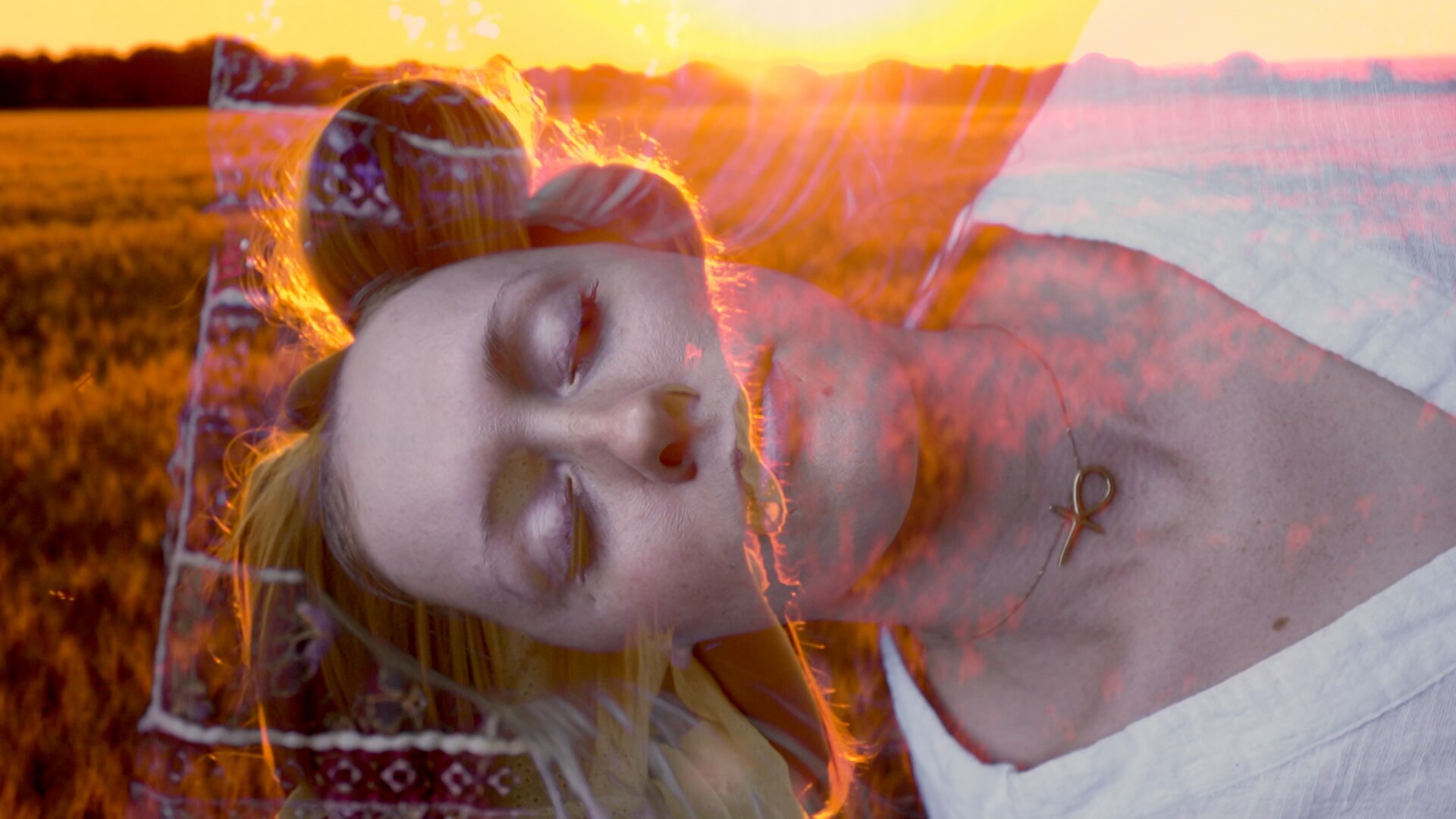 A woman laying down with her eyes closed hallucinating a woman carrying a child in a field bathed in warm orange light. 