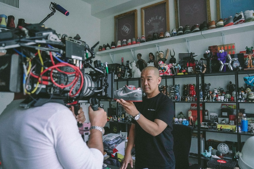 一名穿黑色衣服的男子对着摄像机展示一款灰色的球鞋。